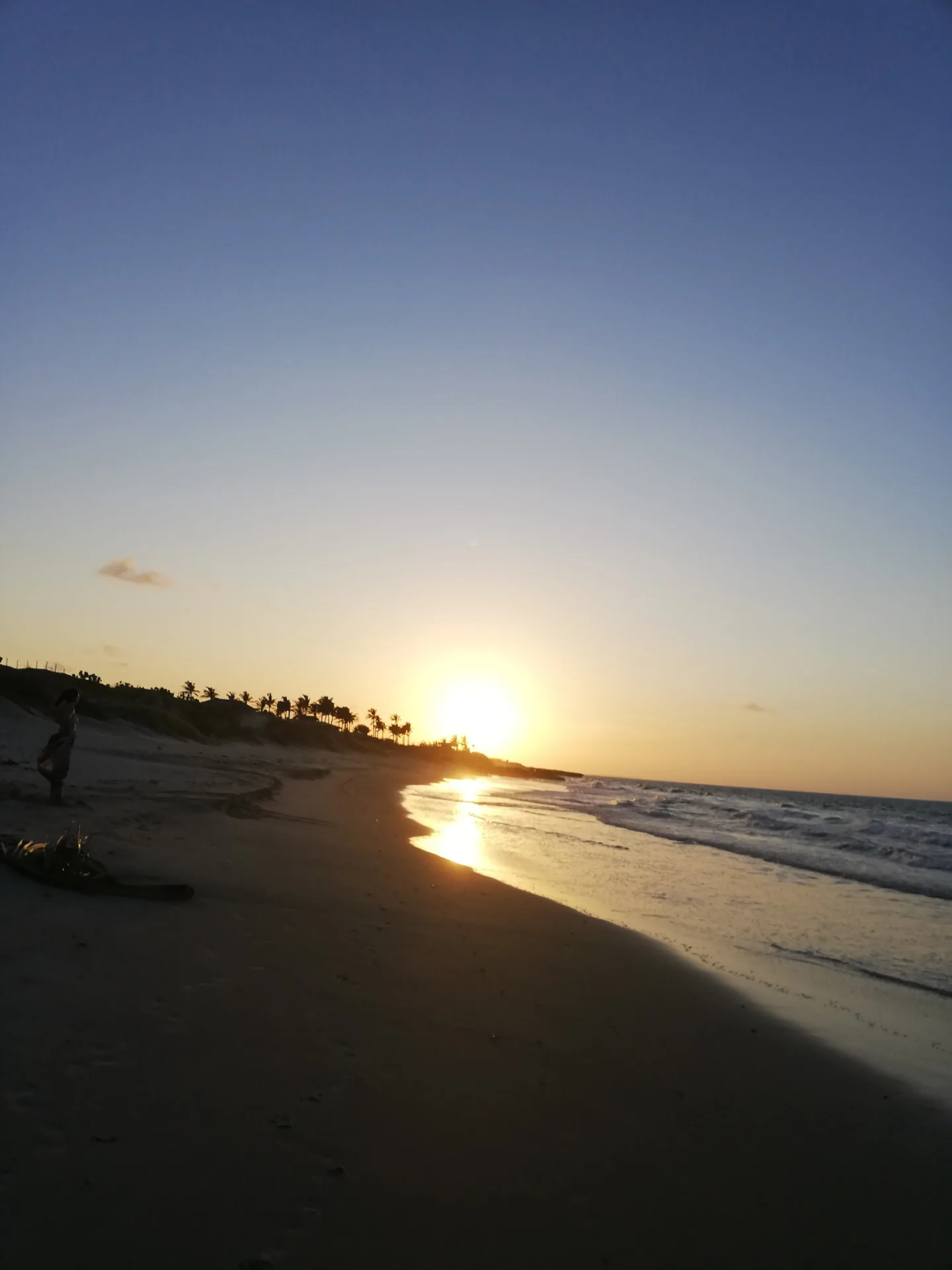 Sol se pondo sobre a praia, refletido na areia molhada