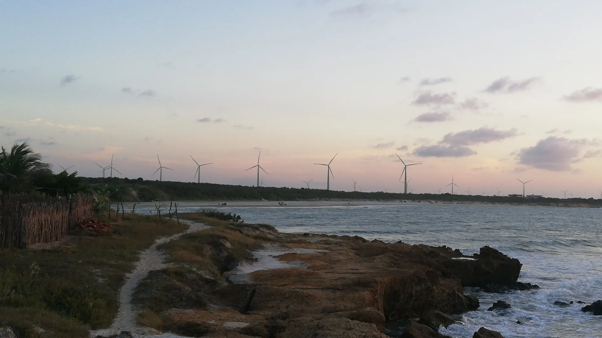 Trilha sobre as falésias baixas, com o mar e as eólicas ao fundo
