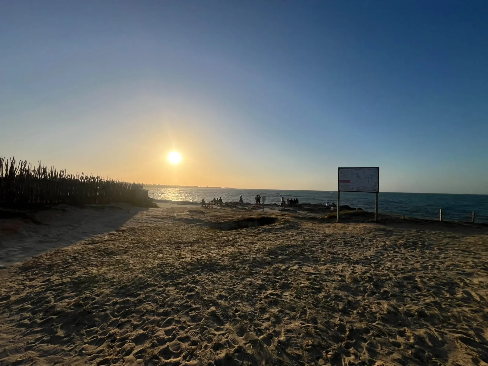 Fim de tarde na falésia, com o sol sobre o mar e visitantes ao longe