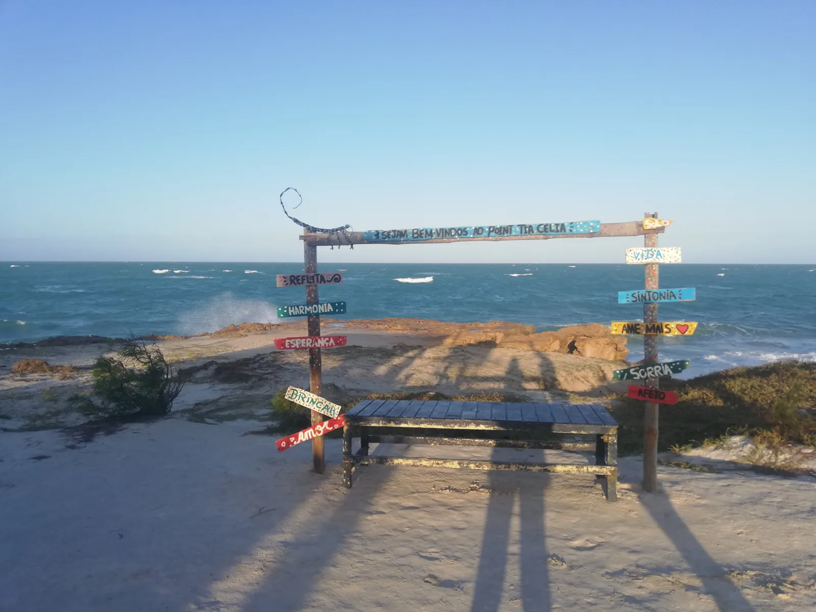 Mirante com banco e placas coloridas sobre as pedras, de frente para o mar
