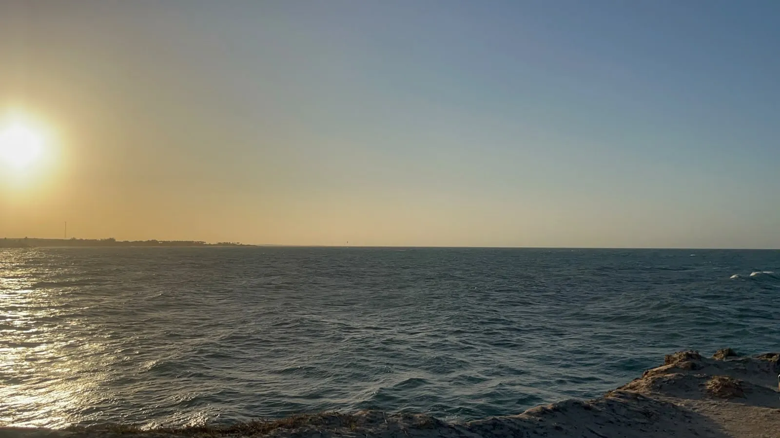 Sol no canto do céu e ondas batendo nas pedras