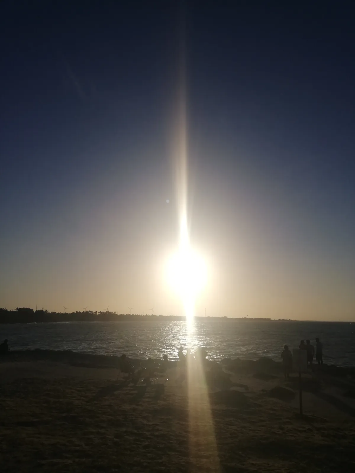 Raio de sol sobre a praia, com silhuetas de visitantes ao longe