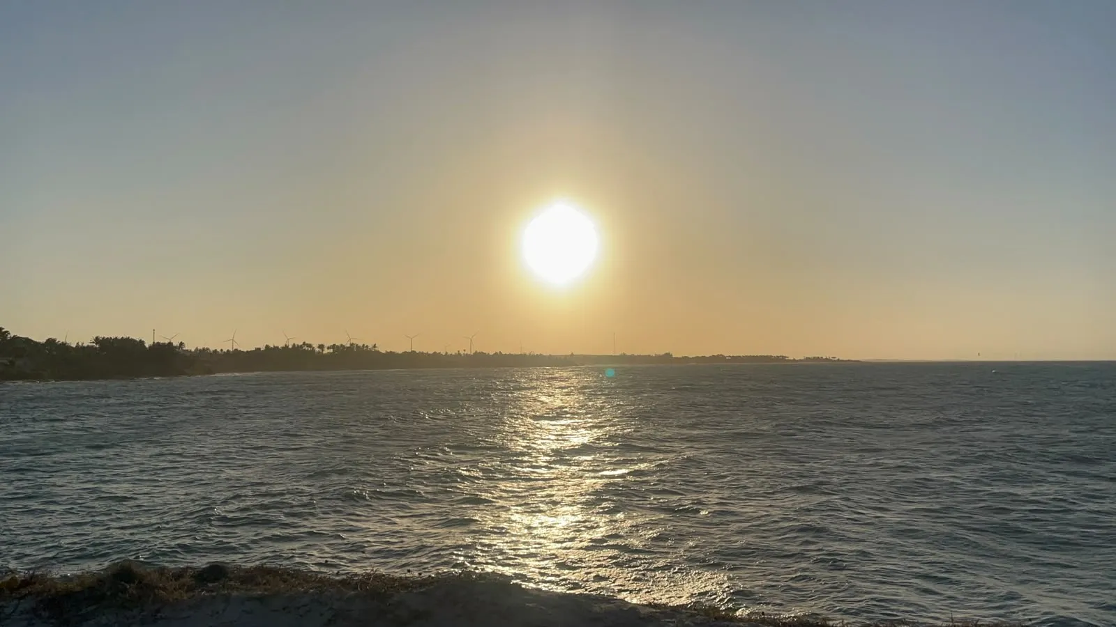Sol descendo sobre o mar, com a linha da costa ao fundo